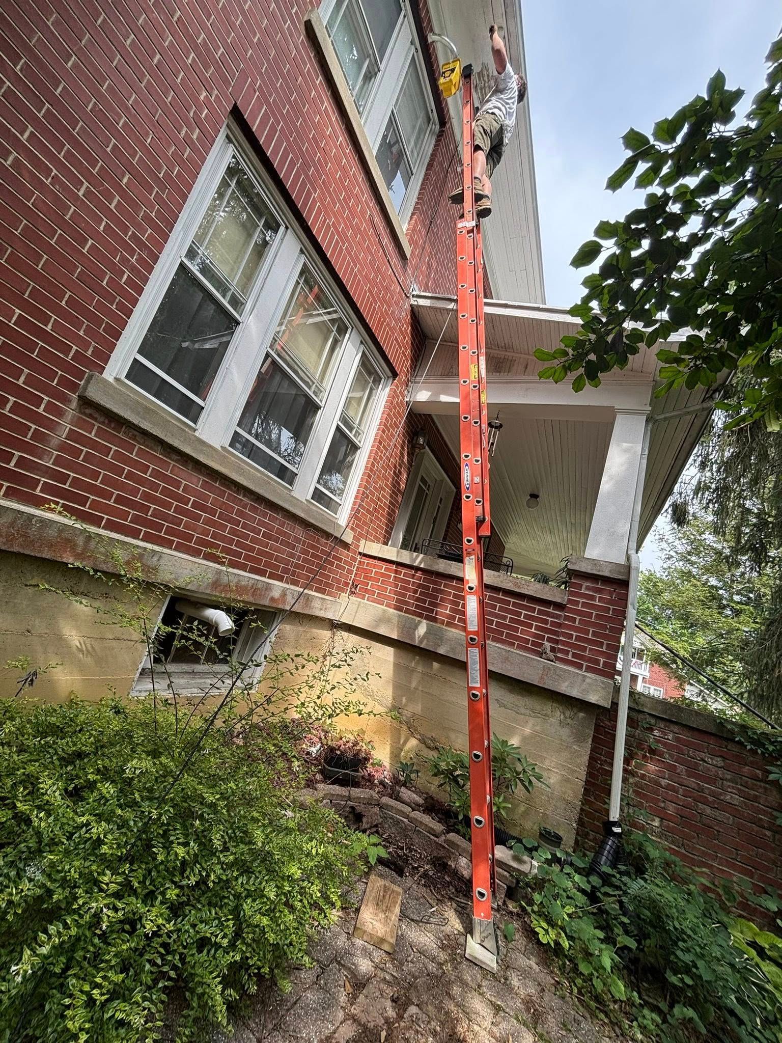 Person on tall ladder working on brick building exterior.