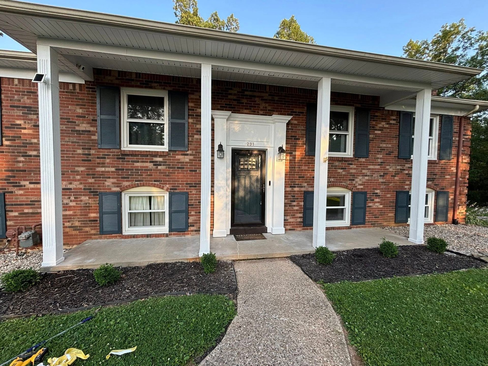 Red brick house with white porch columns, dark blue shutters, and a stone walkway.