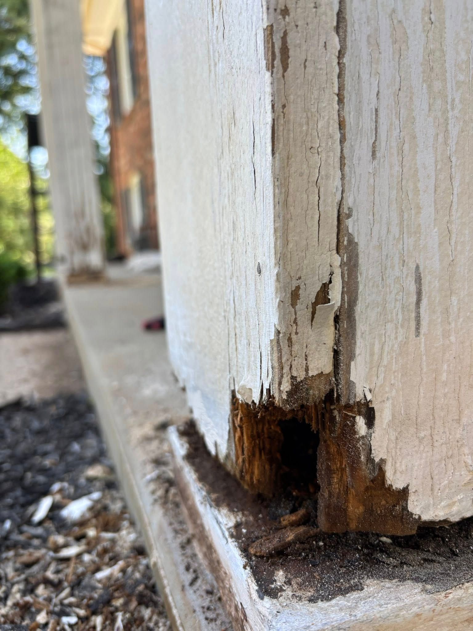 Damaged white painted wooden porch post with rotted wood at the base.