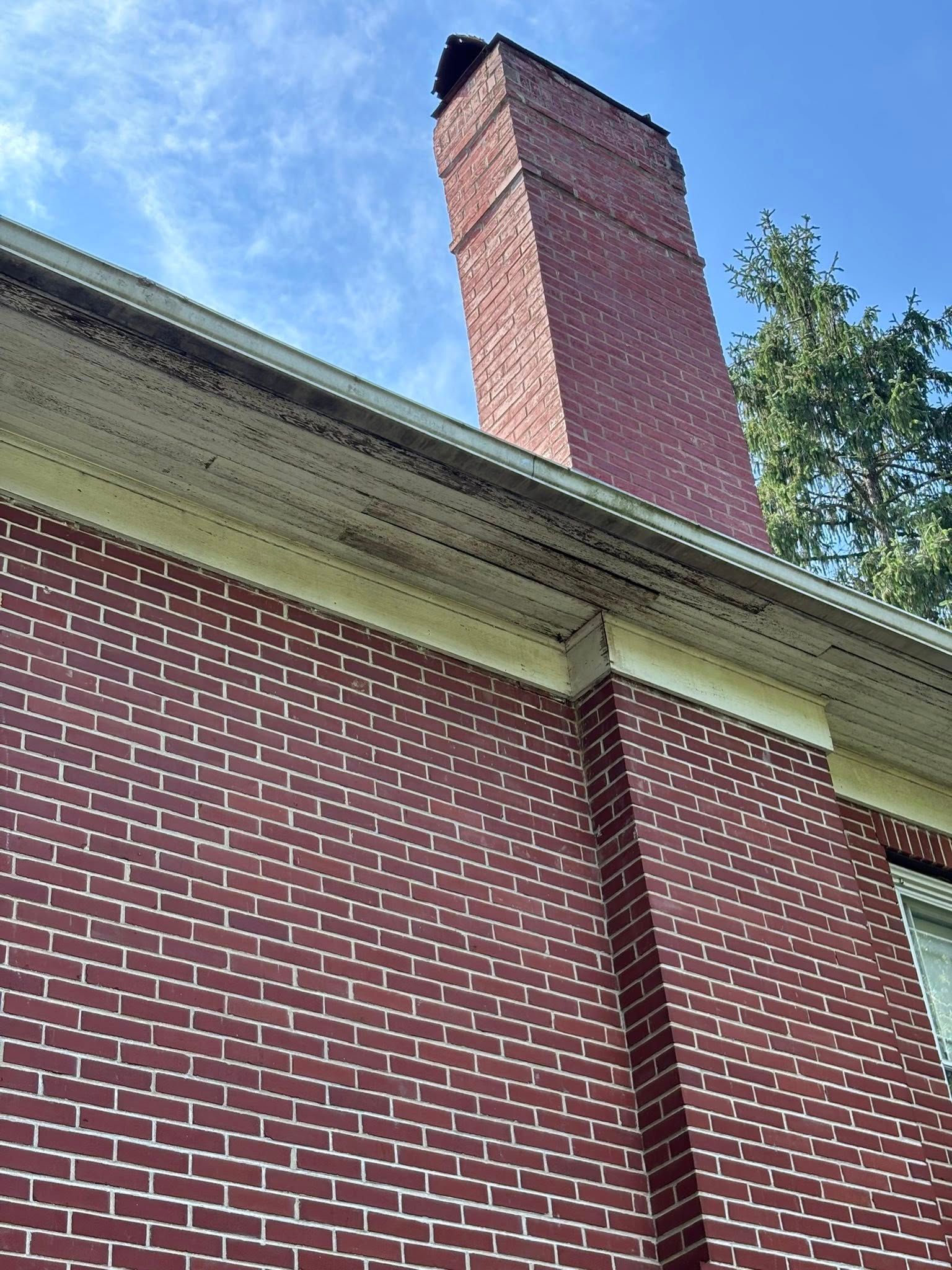 Red brick chimney against blue sky, attached to red brick house.