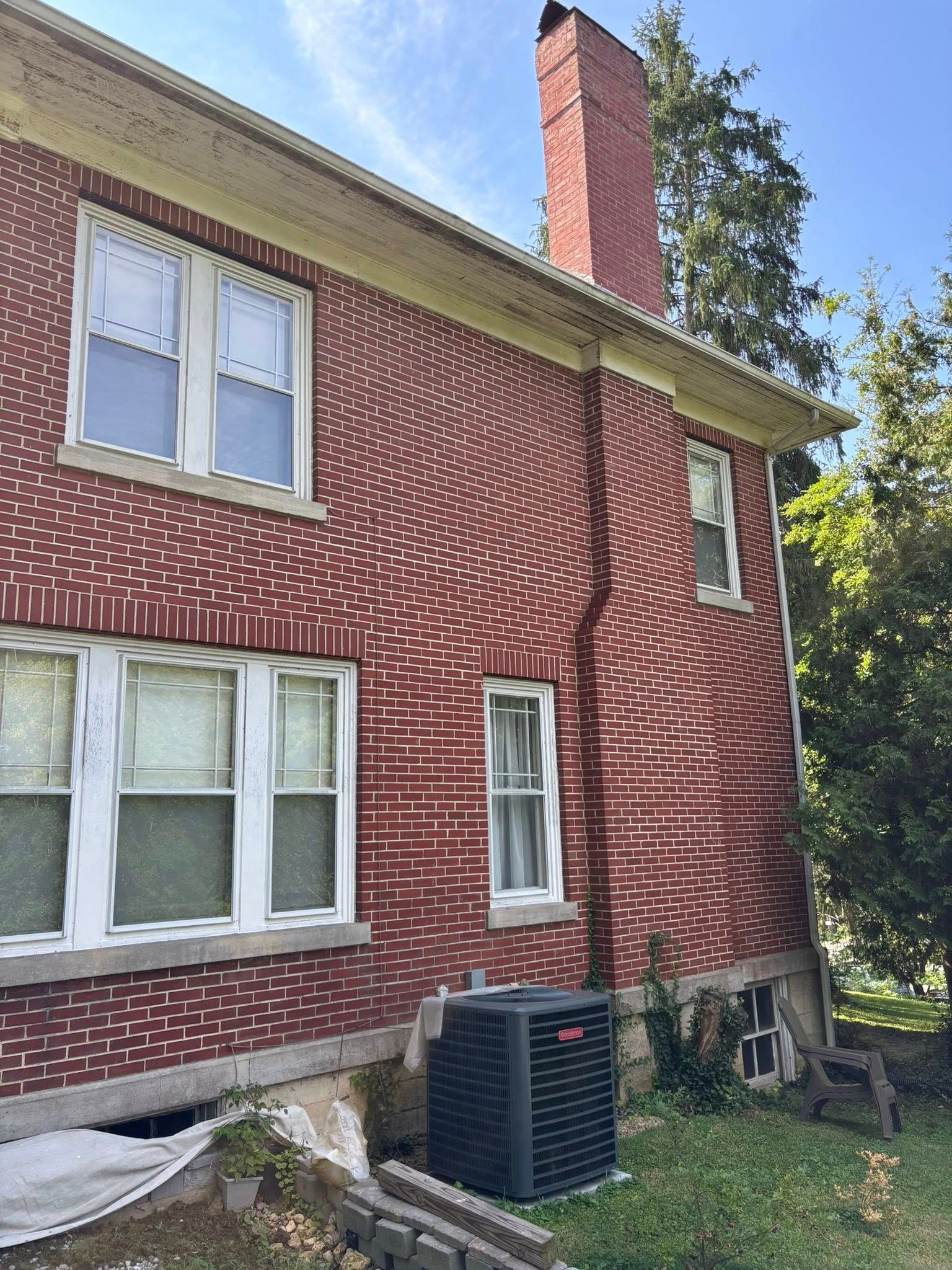 Red brick building with white-trimmed windows, a chimney, and an AC unit.