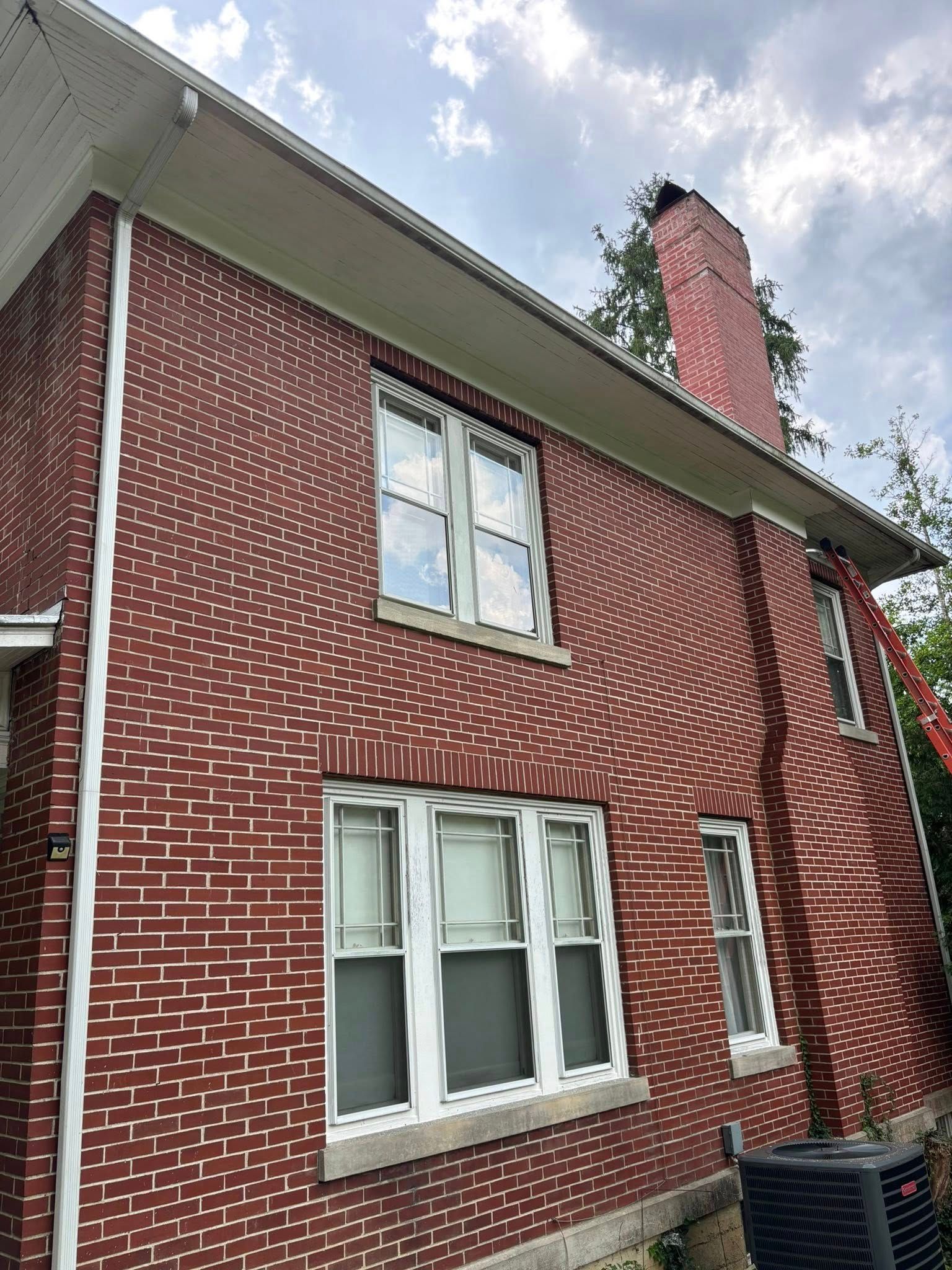Red brick building with white trim, windows, and a chimney against a cloudy sky.