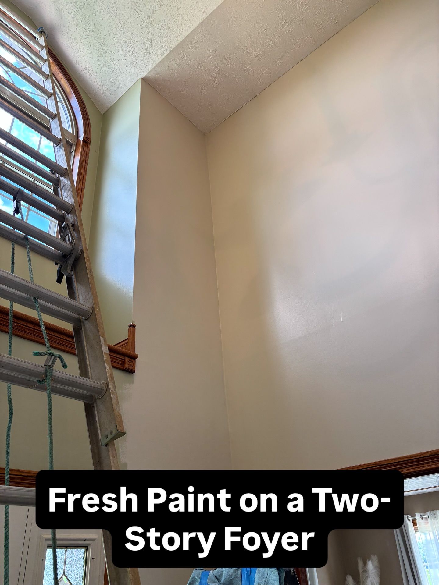 Two-story foyer with fresh paint; a ladder is positioned near an arched window.