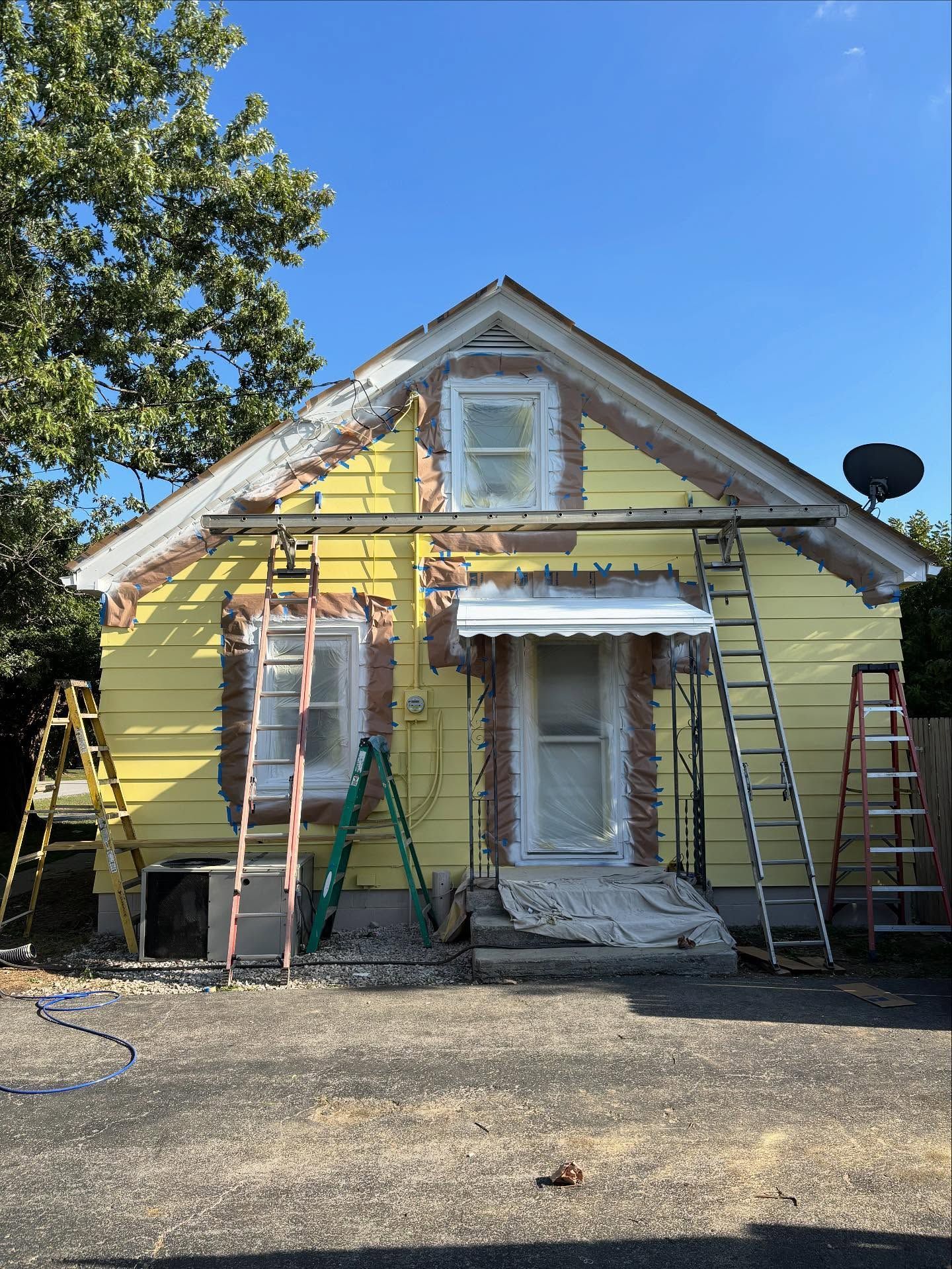 House exterior being painted, yellow siding, ladders, scaffolding, and covered door.