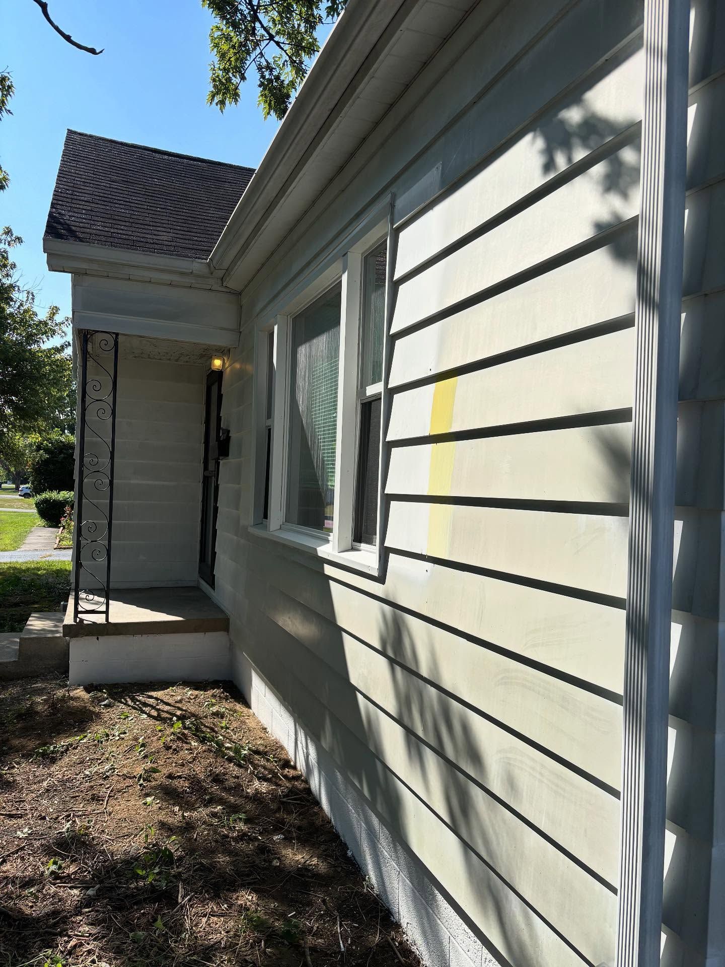 Side view of a light-colored house with a small porch, window, and yellow stain on the siding.