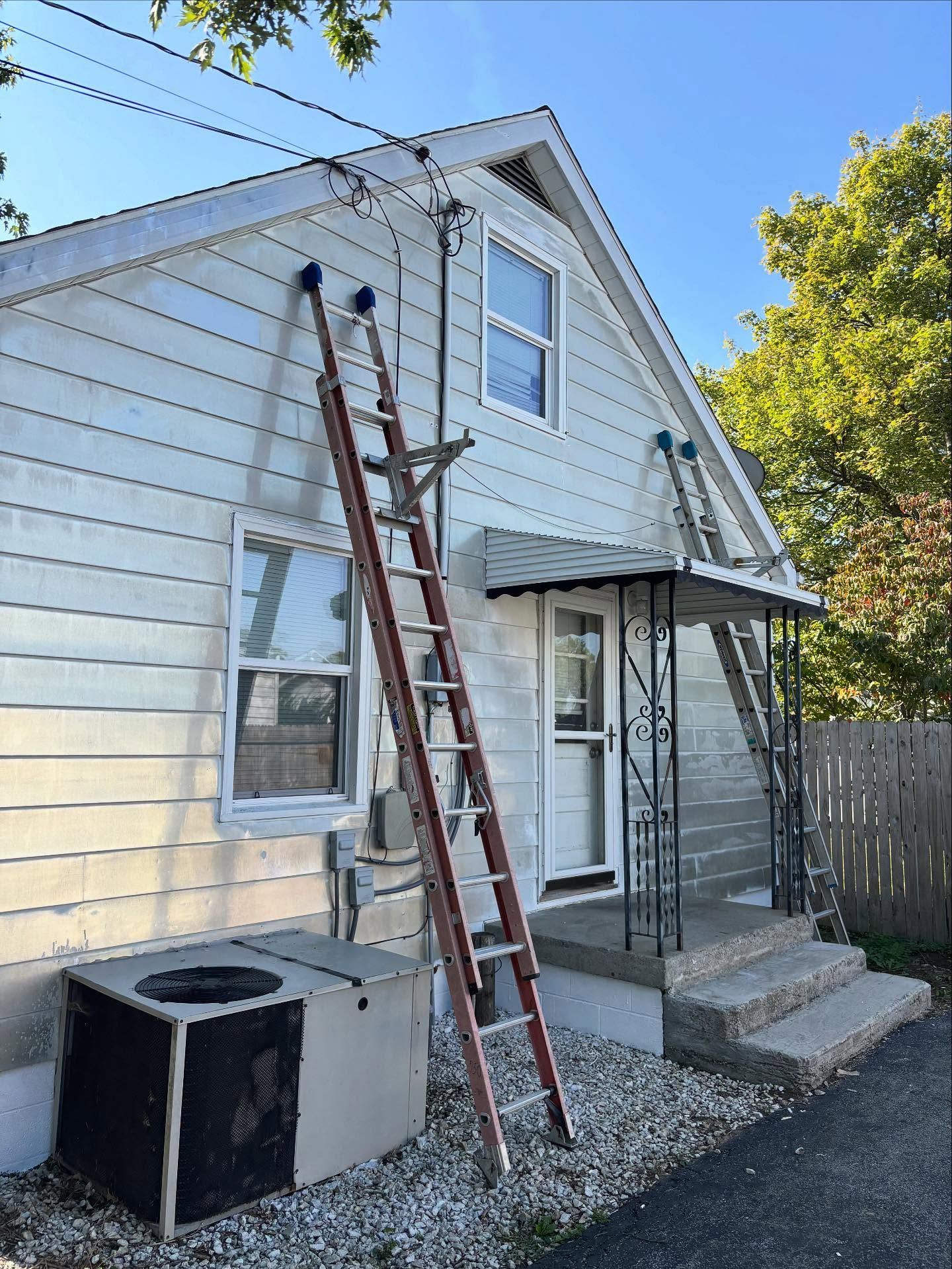 Two ladders leaning against a house with light siding and an awning over the front door.