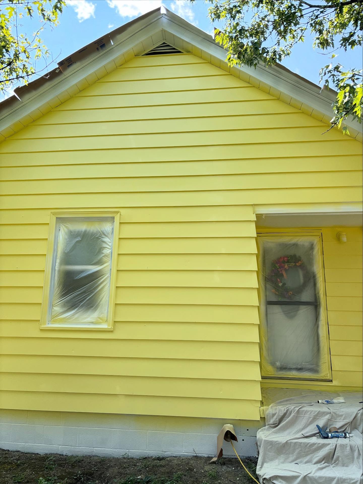 Yellow house with covered window and door, freshly painted exterior, under blue sky.