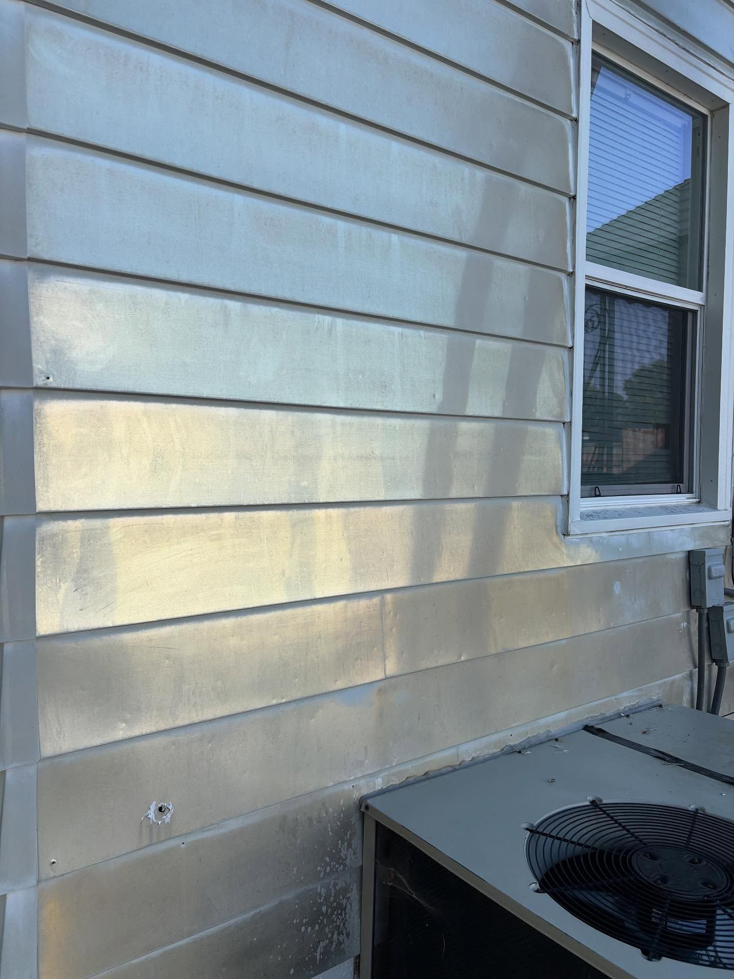 Silver-painted siding on a house next to a window and air conditioning unit.