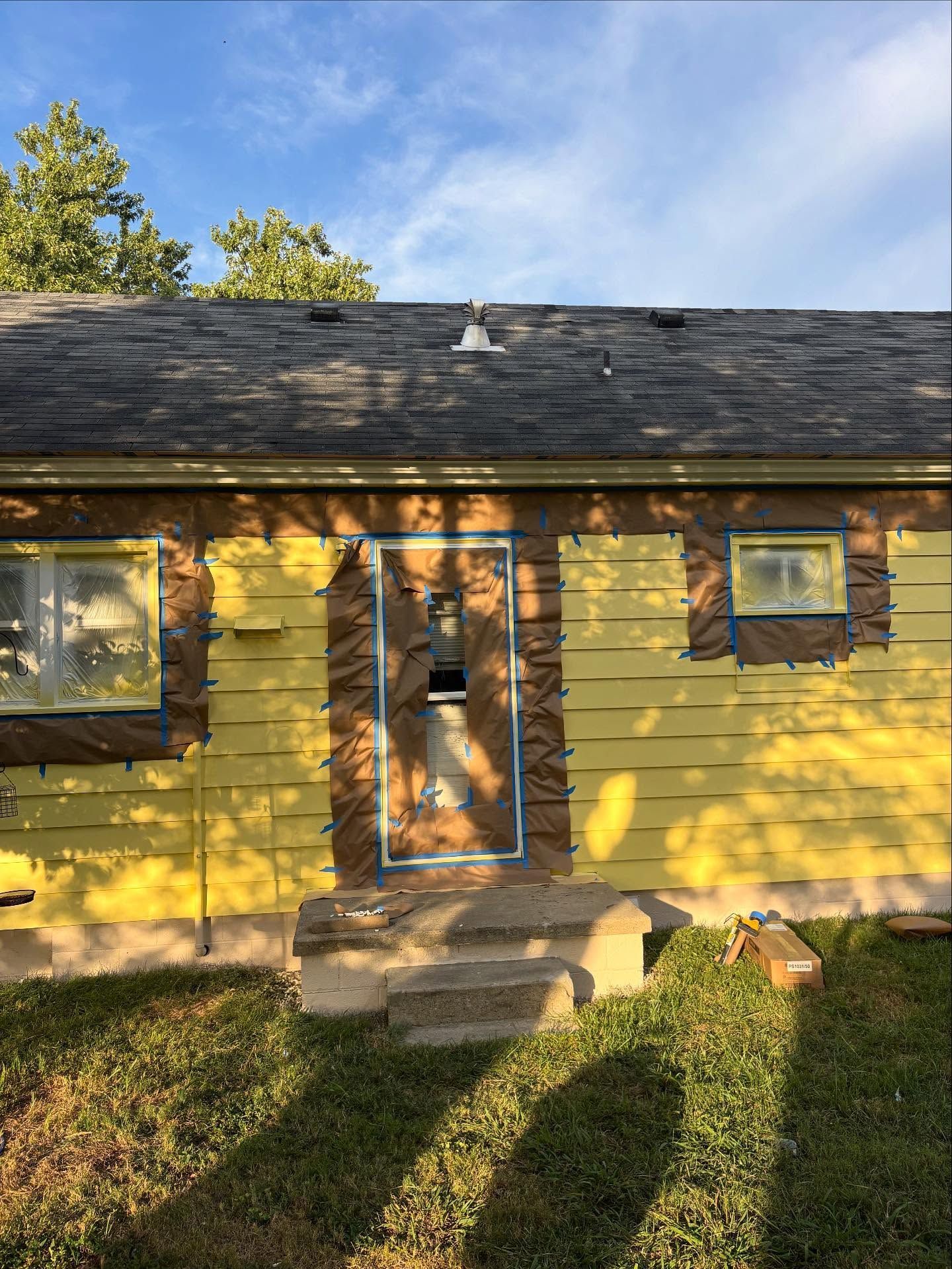 House exterior under construction, yellow siding with exposed areas, roof damage, steps.