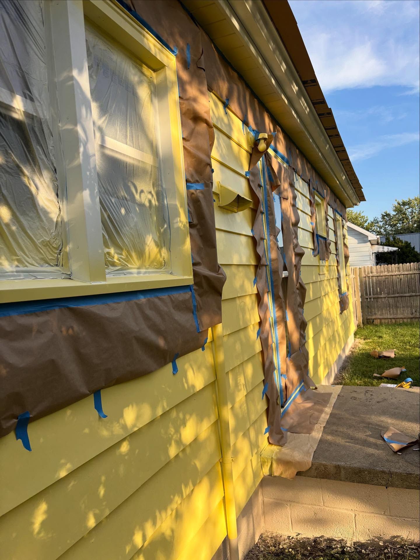House exterior being painted yellow, windows and trim taped off.