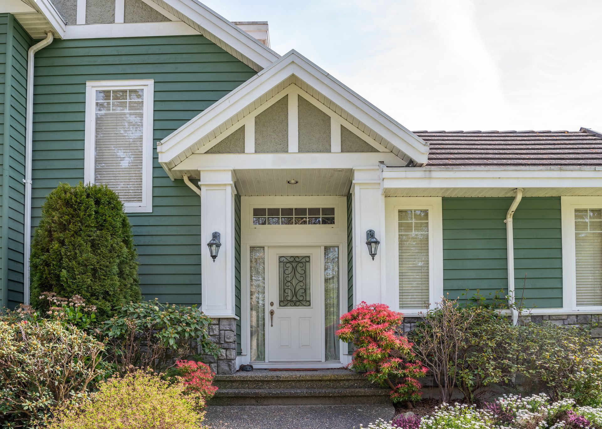 White brick house with black door, steps, and railing. Landscaping with plants and stone.