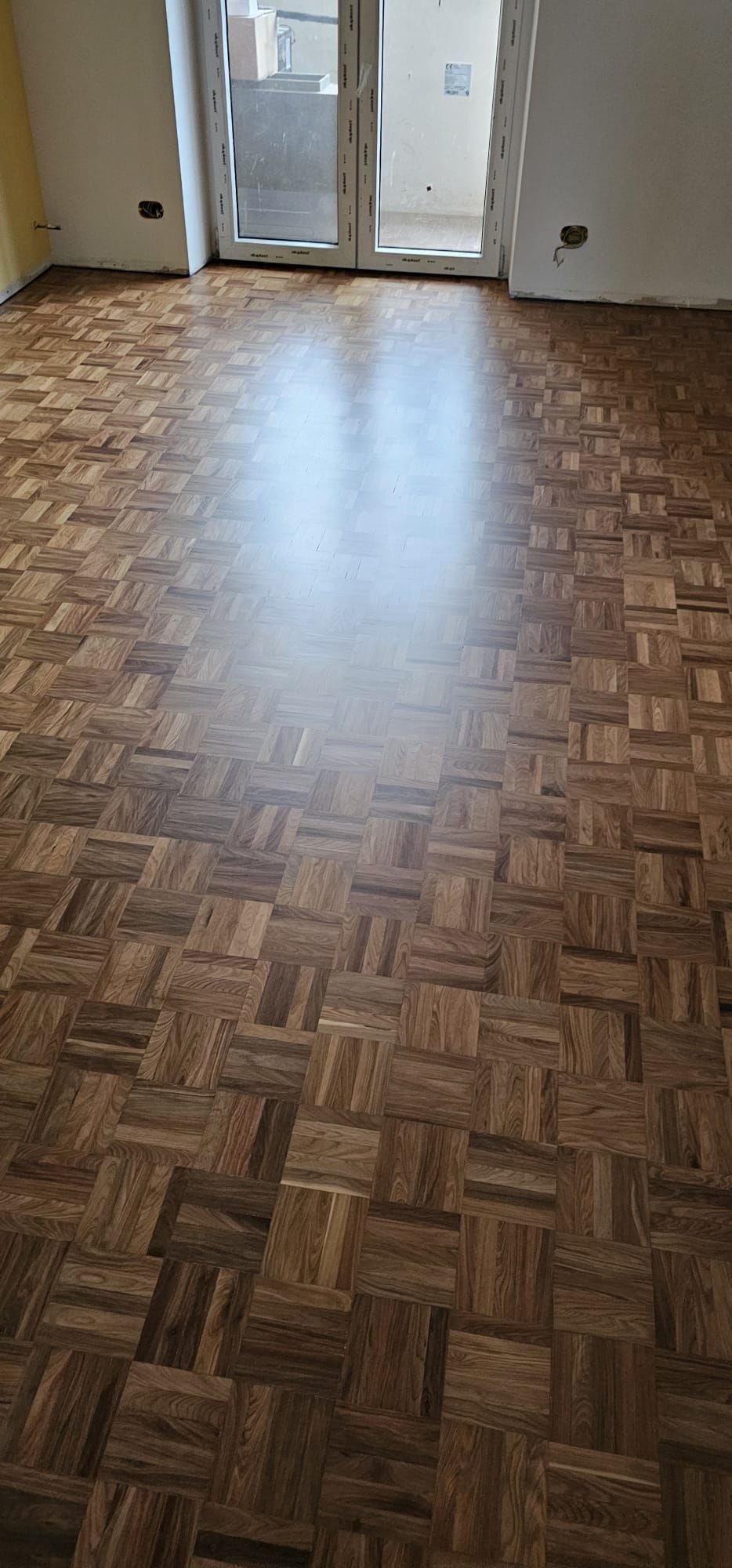 Pavimento in parquet in una stanza con porta a vetri chiusa e pareti bianche.