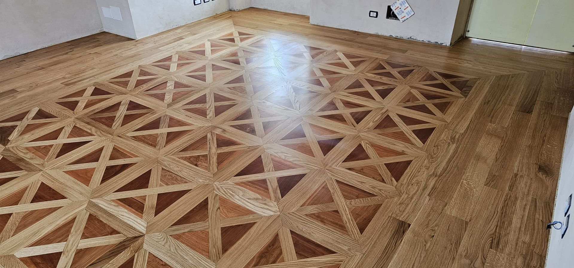 Pavimento in parquet di legno con motivo geometrico ripetuto di triangoli e quadrati.