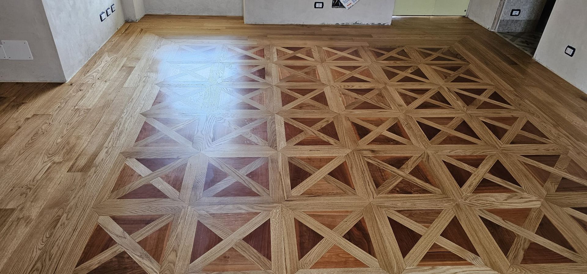 Pavimento in legno con motivo geometrico. Il design è caratterizzato da tonalità marroni e legno chiaro.