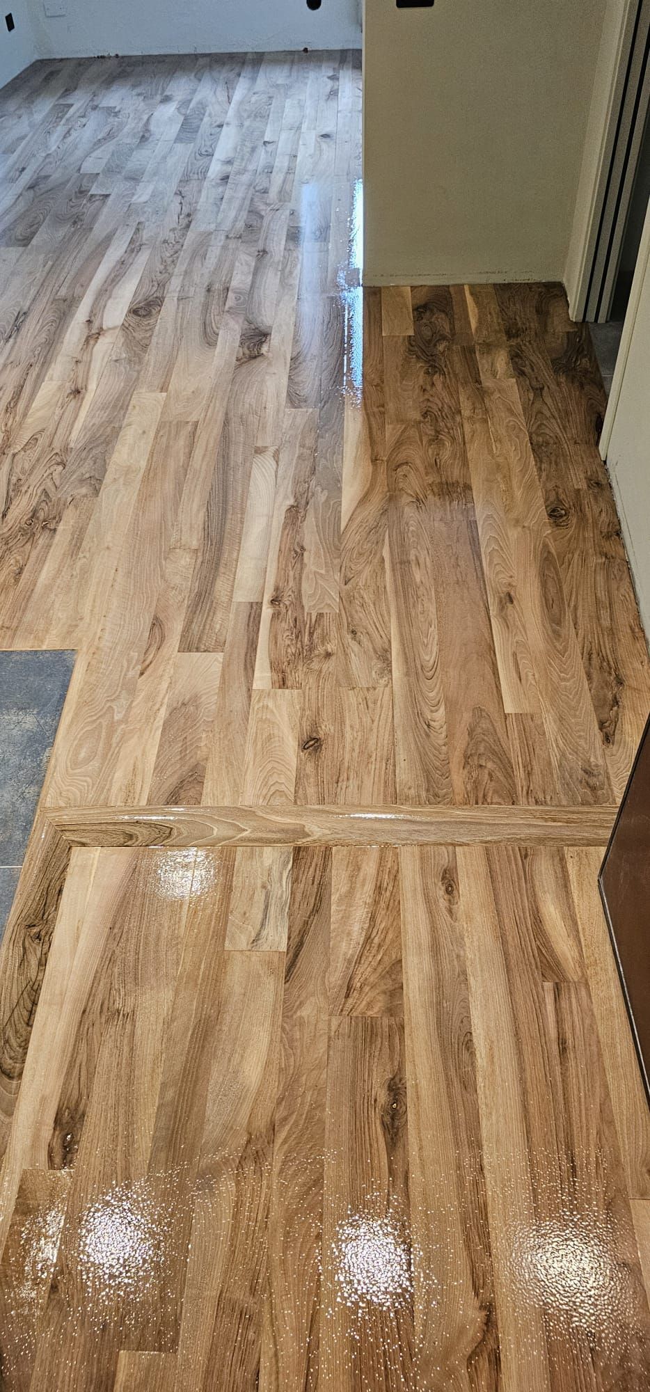 Pavimento in legno con assi marrone chiaro. Diversi punti luce bianchi si riflettono sulla superficie lucida.