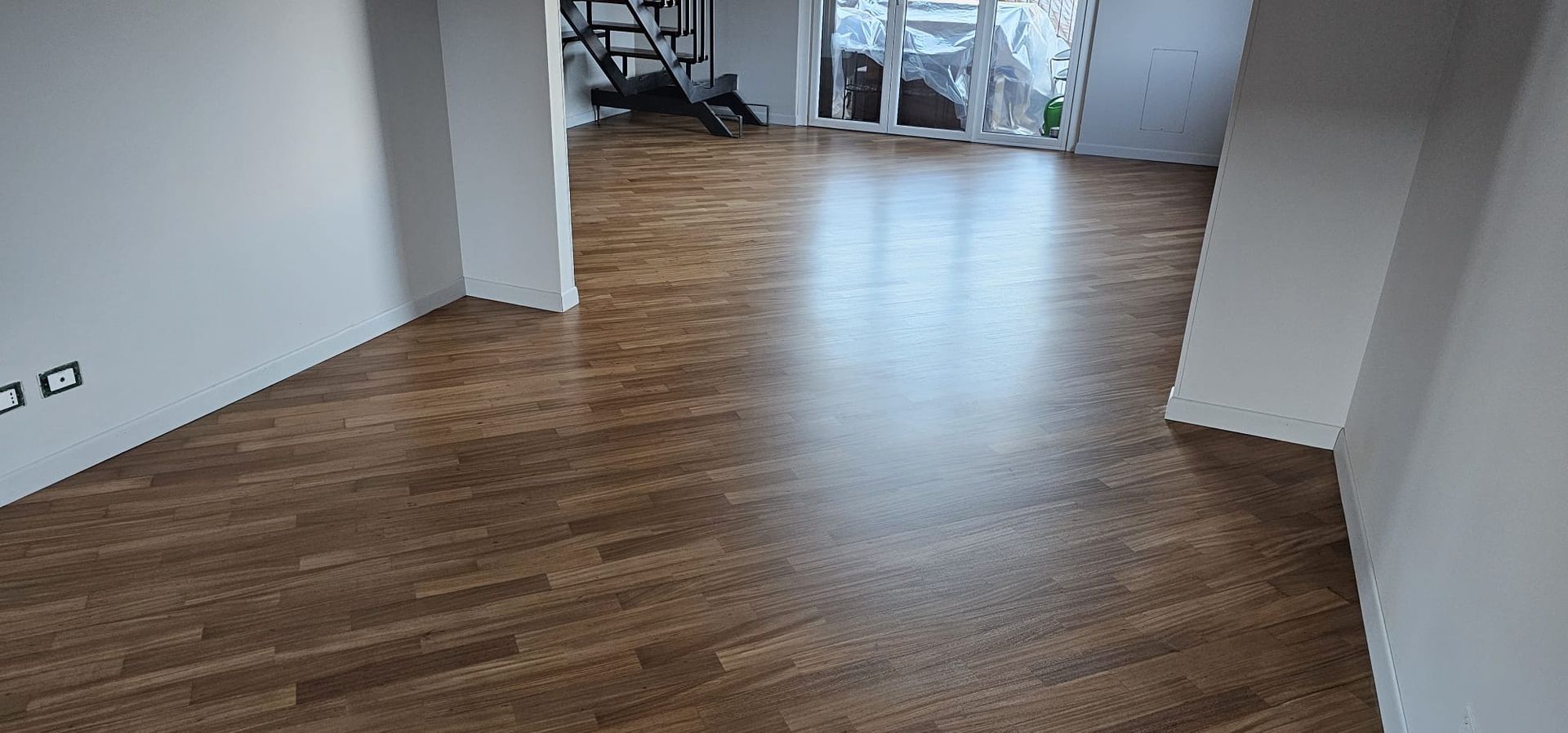 Pavimento in legno marrone in una stanza con pareti bianche. La luce del giorno filtra da un'apertura.