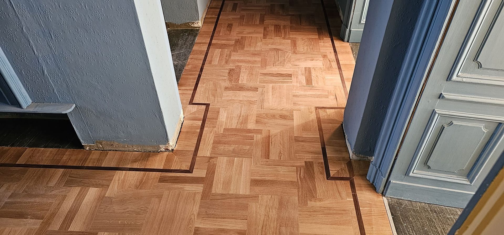 Corridoio con parquet in legno e bordo scuro tra le pareti blu.