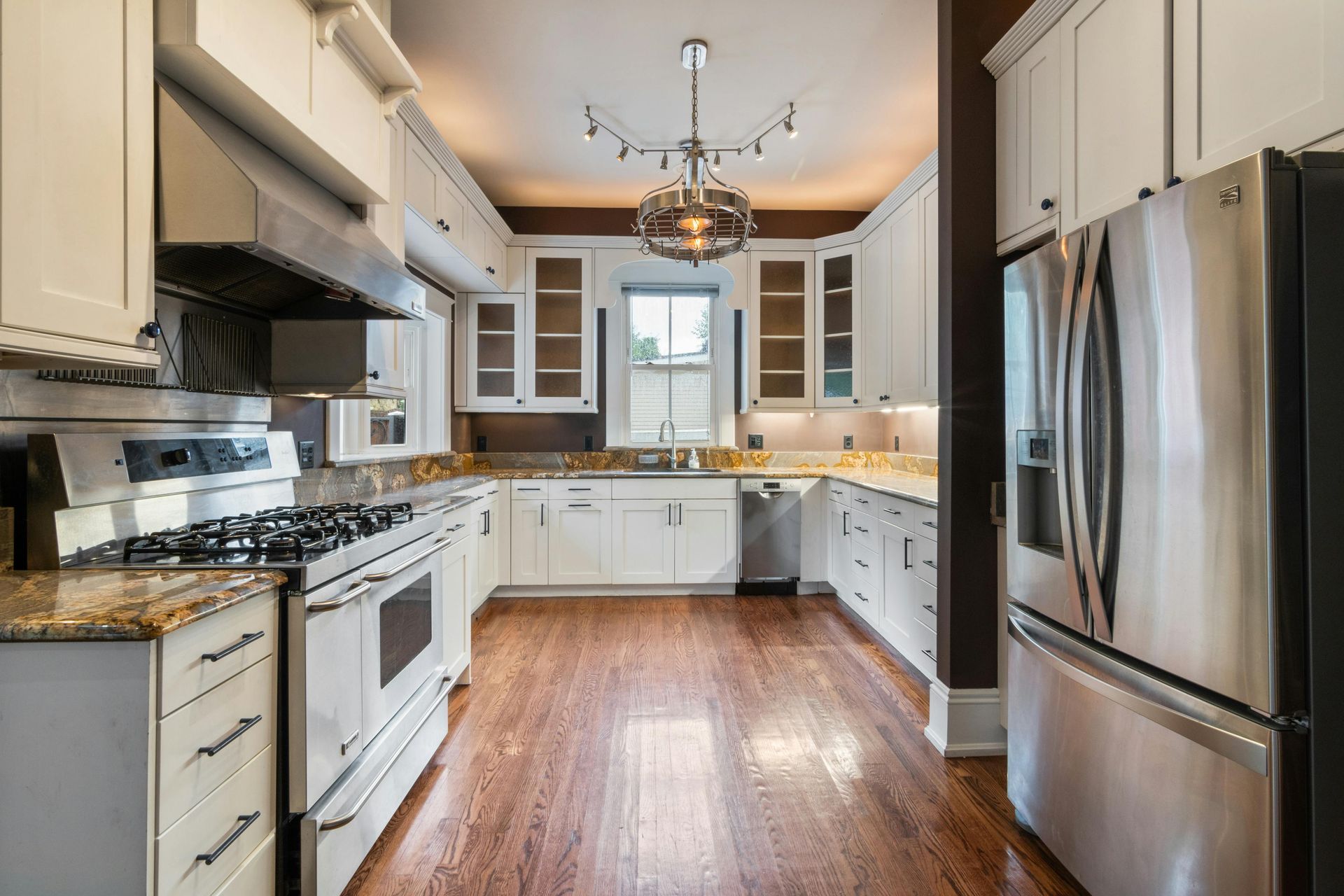 A U-shaped kitchen with white cabinets, stainless steel appliances, granite countertops, and hardwood flooring.