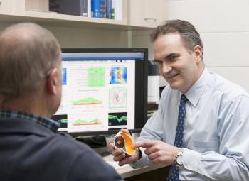 A man is holding a model of an eye while talking to another man.