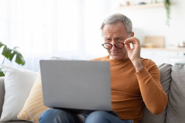 An older man is sitting on a couch using a laptop computer.