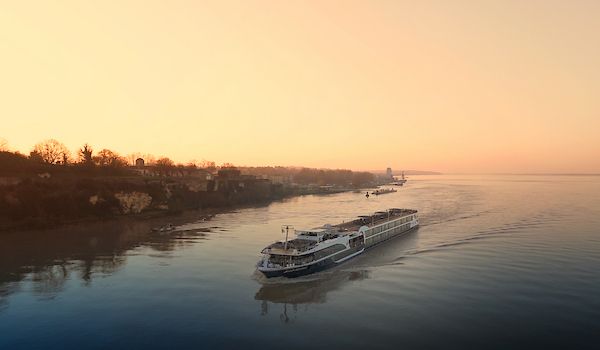 River cruise ship sailing on a calm river at sunrise, with golden sky and shoreline.