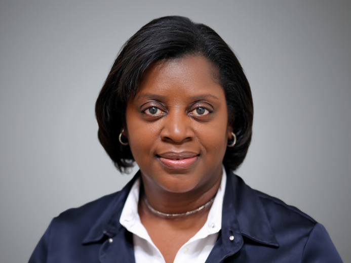 Woman in a dark blue jacket and white shirt, smiling, looking at the camera. Neutral background.