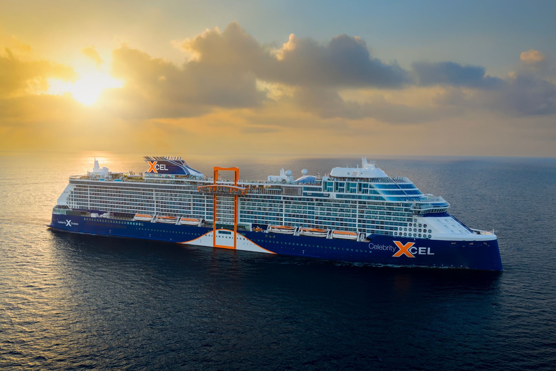 Cruise ship on the ocean with blue and white hull, orange structure, and setting sun in the background.
