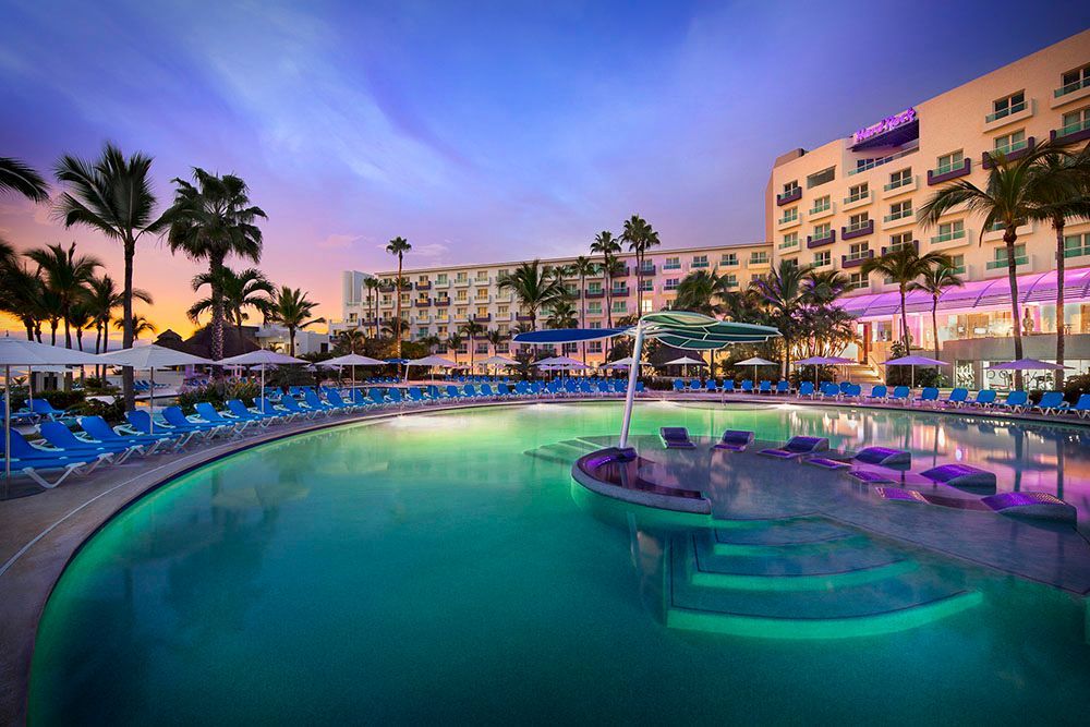 Pool at resort at dusk with palm trees and hotel in background.