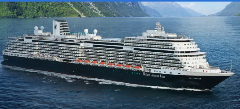 Cruise ship sailing on a body of water with a mountainous landscape in the background.