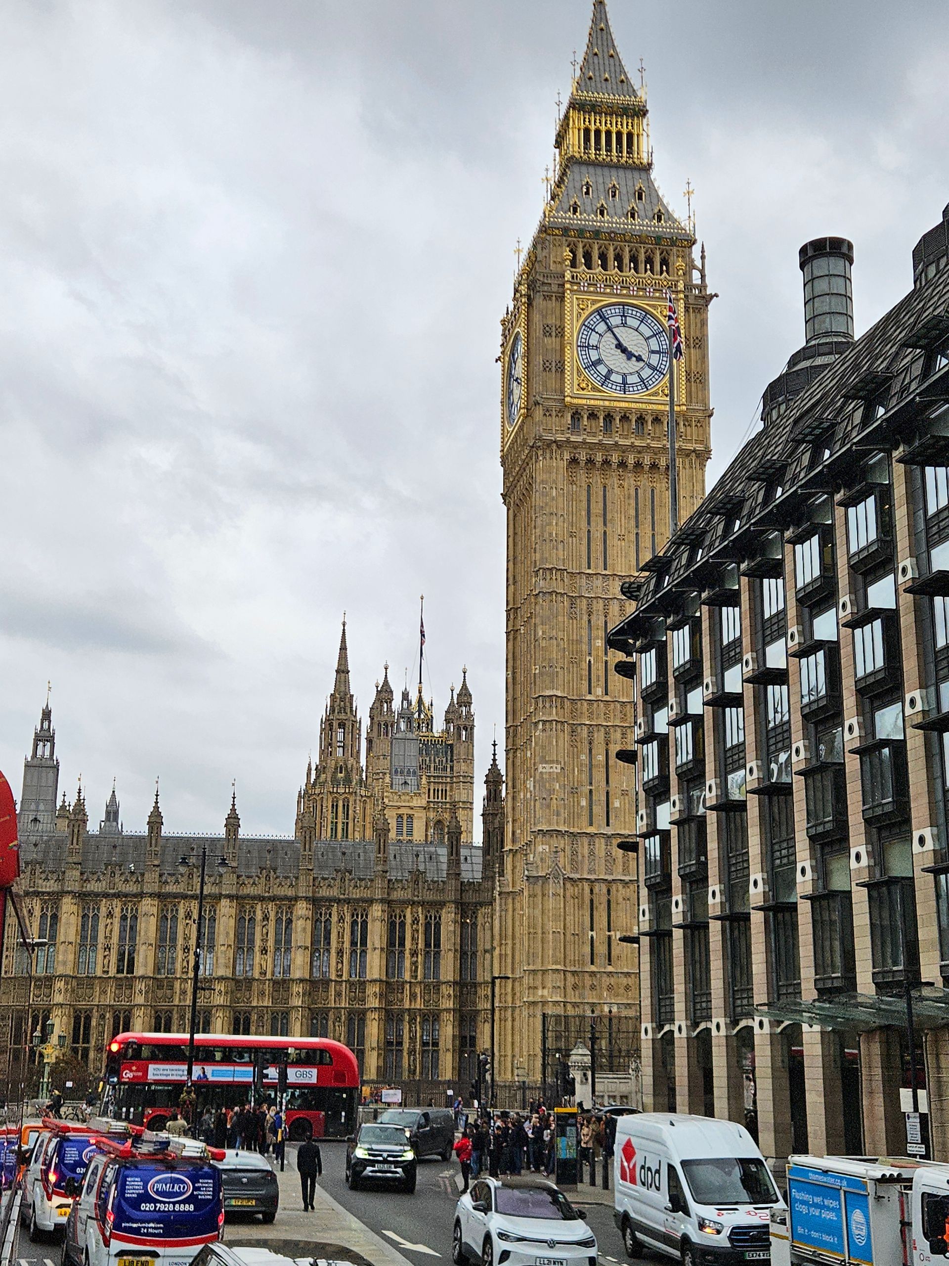 Big Ben clock tower and Houses of Parliament in London, with red bus and traffic on a cloudy day.