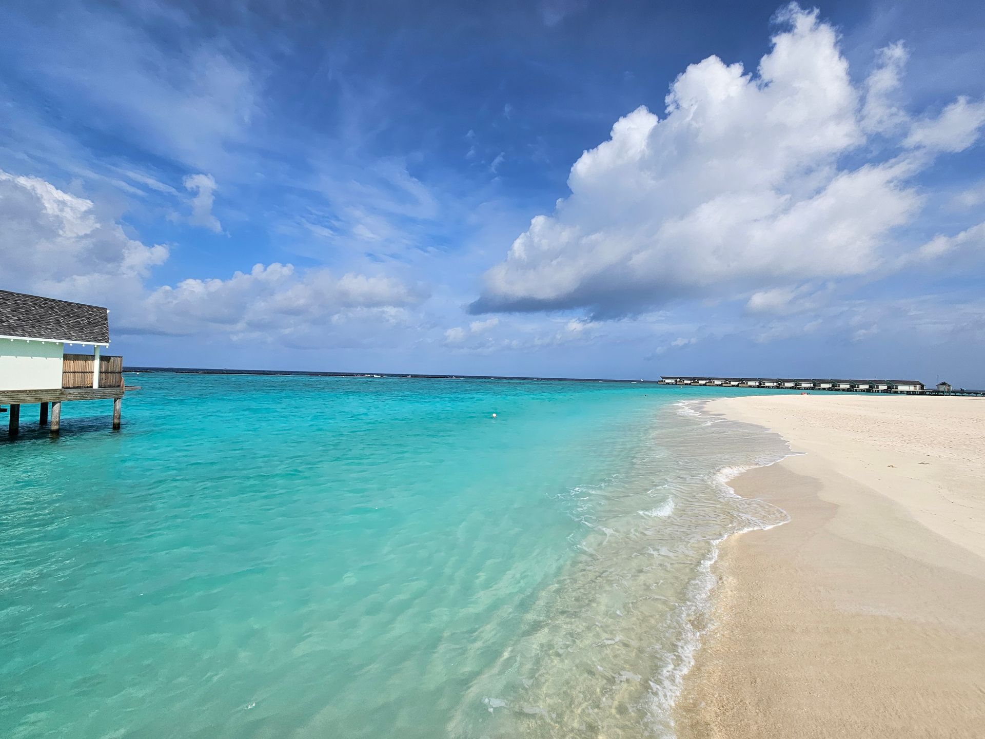 Turquoise ocean meets white sand beach under a blue sky with fluffy clouds.