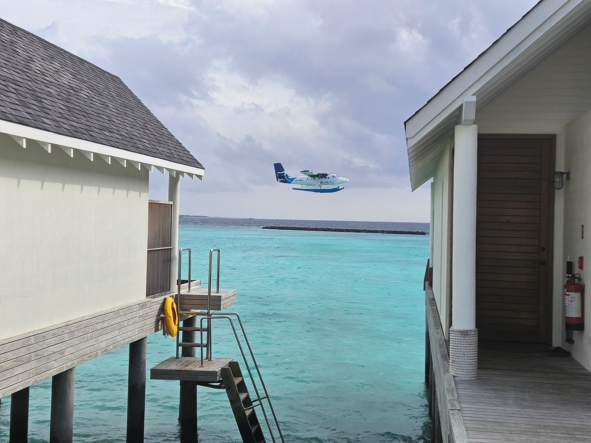Seaplane flying over turquoise water between overwater bungalows.