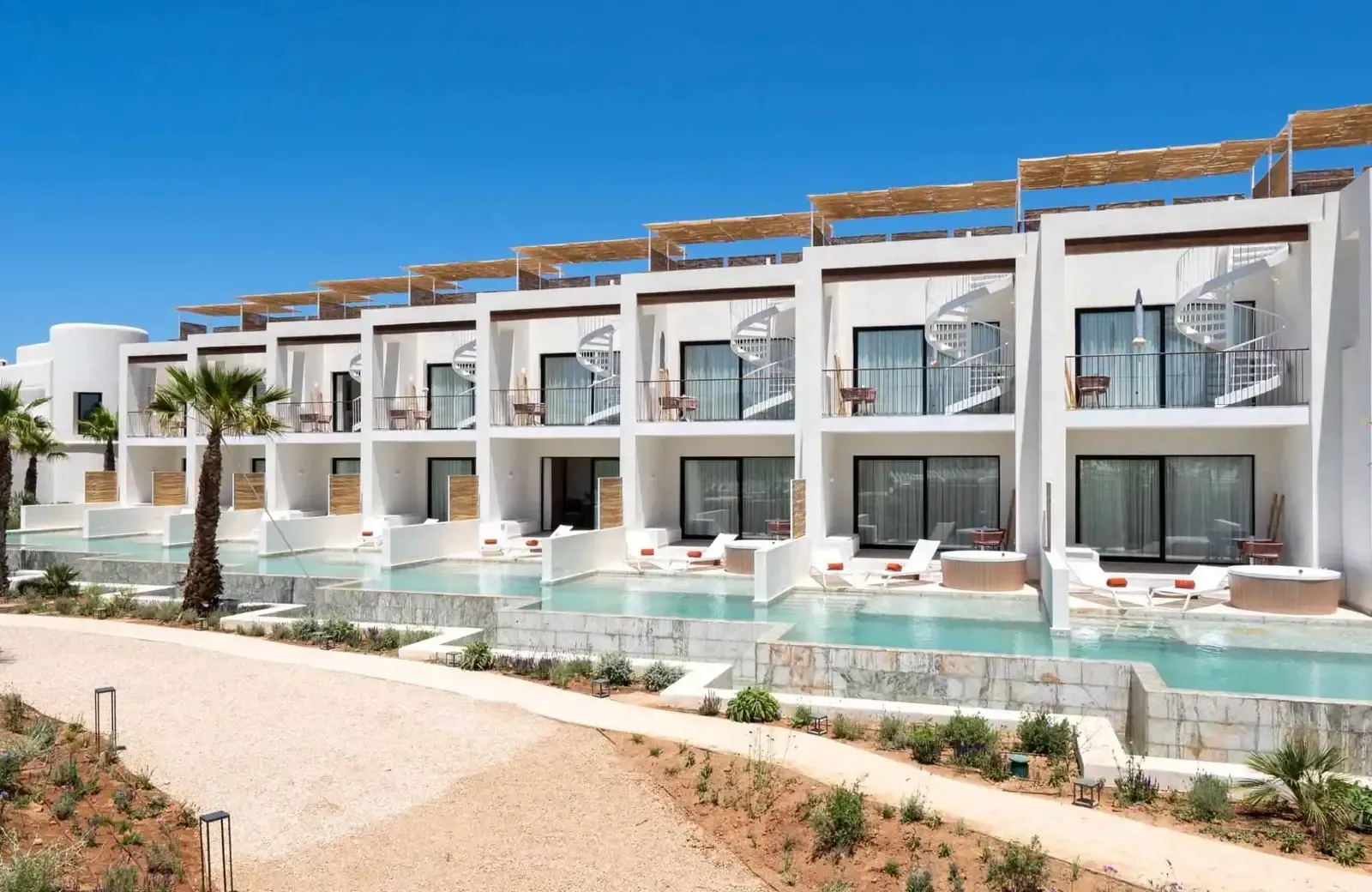White resort building with balconies, pools, and spiral staircases under a blue sky.