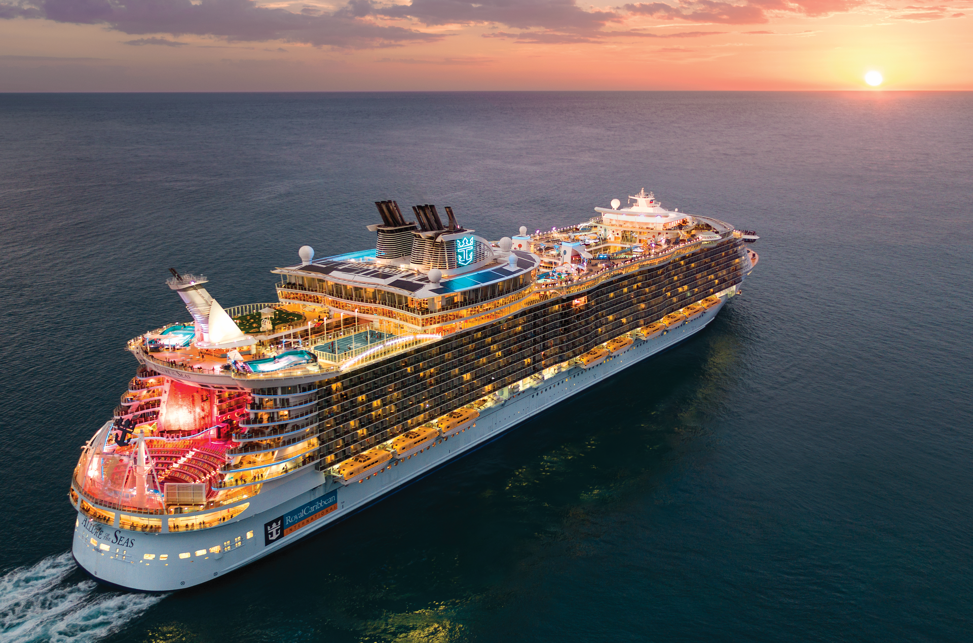 Large cruise ship sailing on ocean at sunset; lit up with many lights.