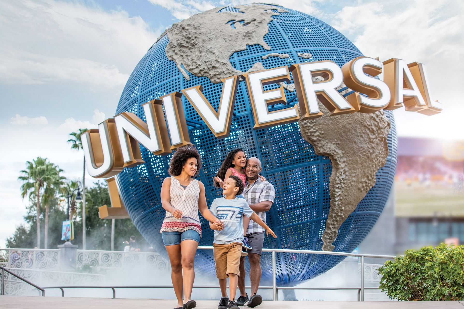 Family in front of the Universal globe. They are walking towards the viewer, smiling in a sunny outdoor setting.