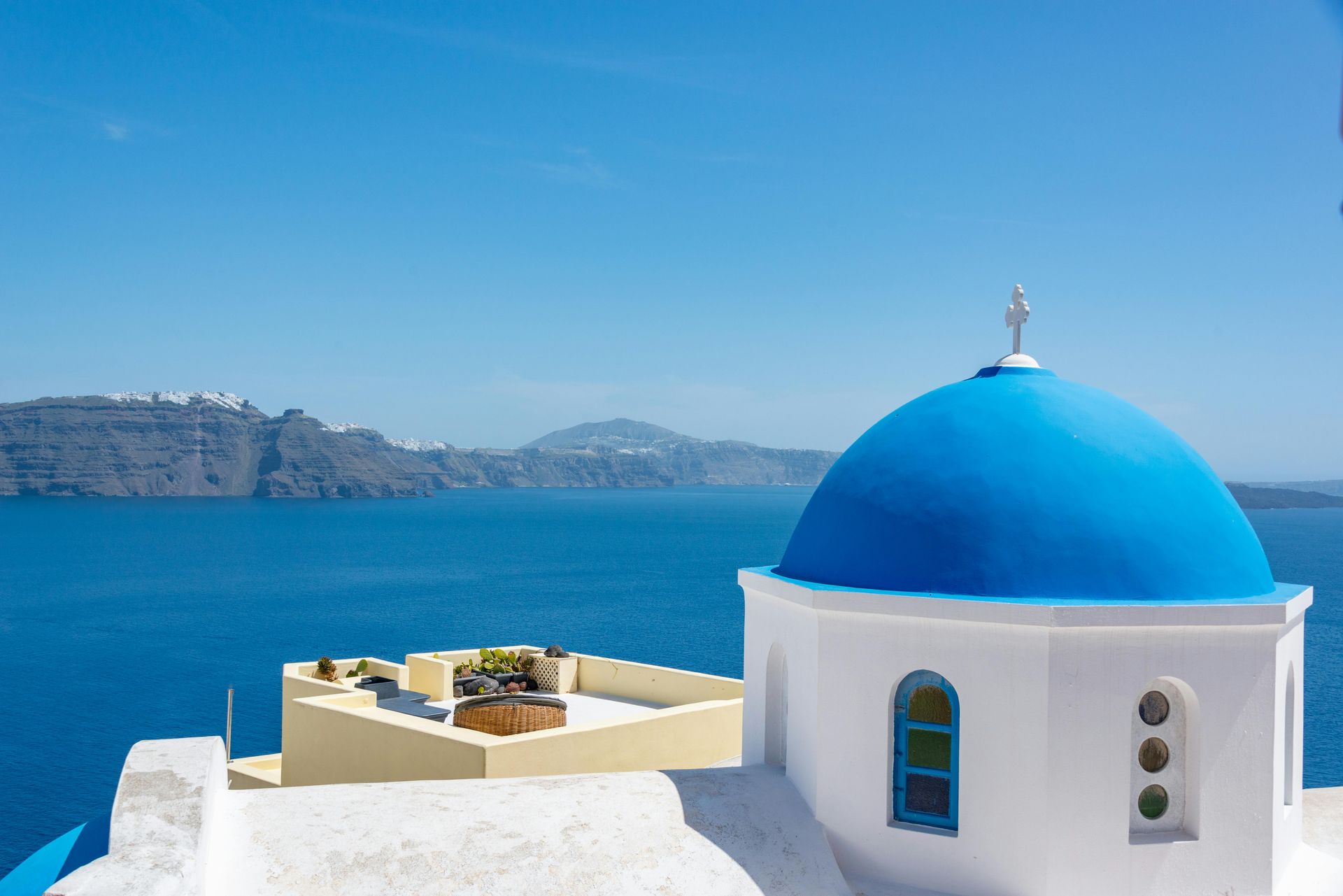 White and blue Greek church with domed roof, overlooking the Aegean Sea.