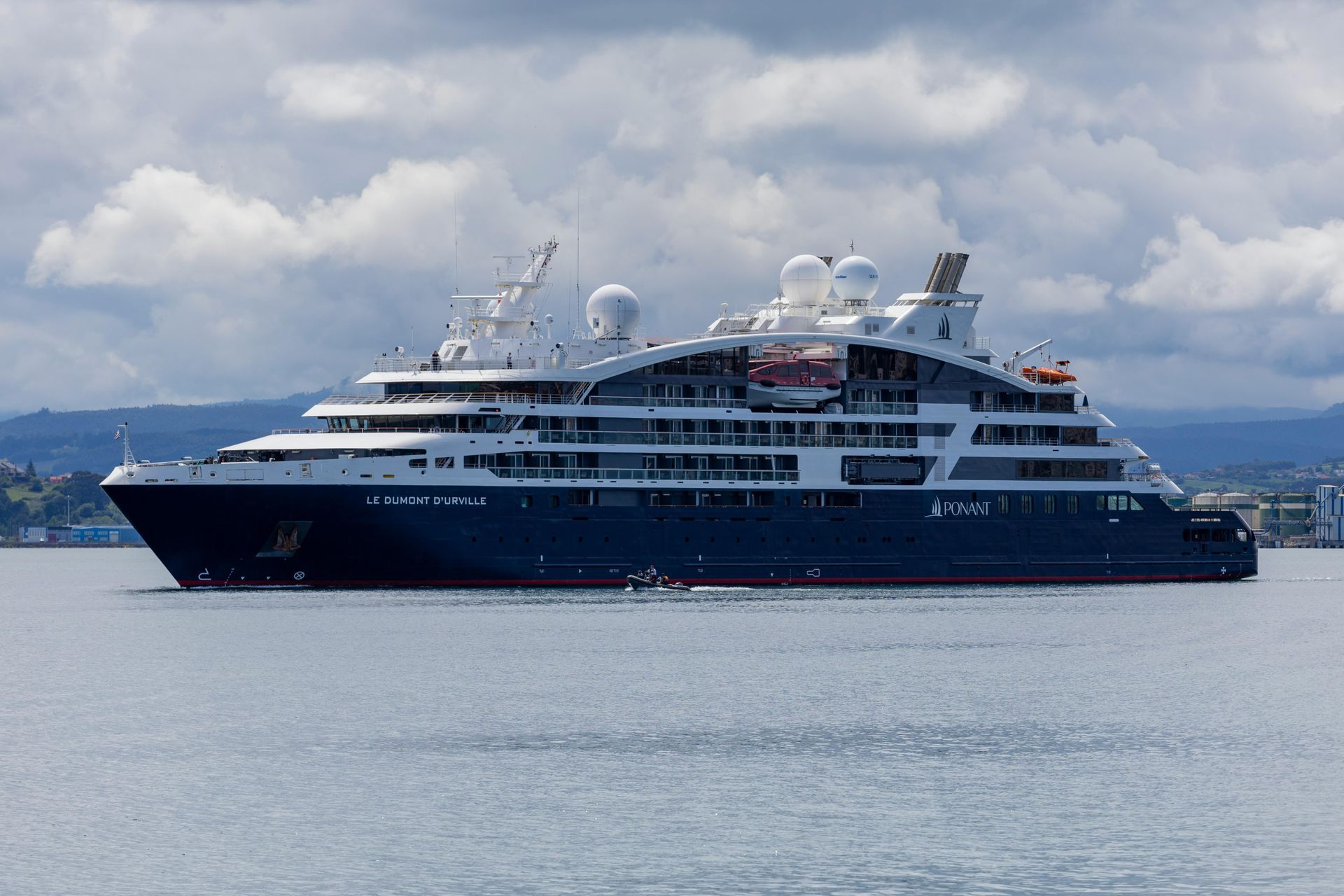 Large dark blue cruise ship on calm water under cloudy sky.