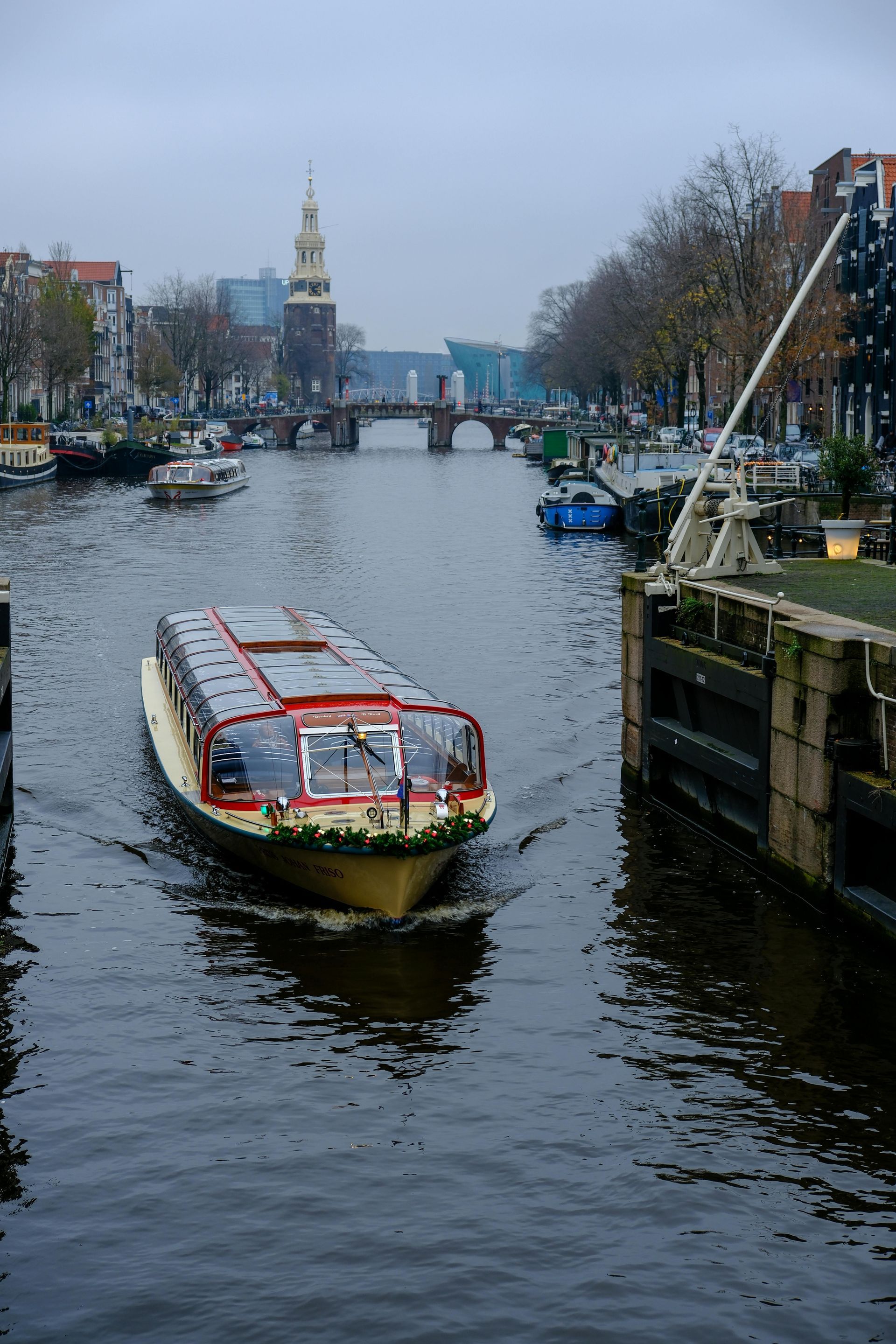 Canal boat in Amsterdam, passing a lock, with a church spire in the background on an overcast day.