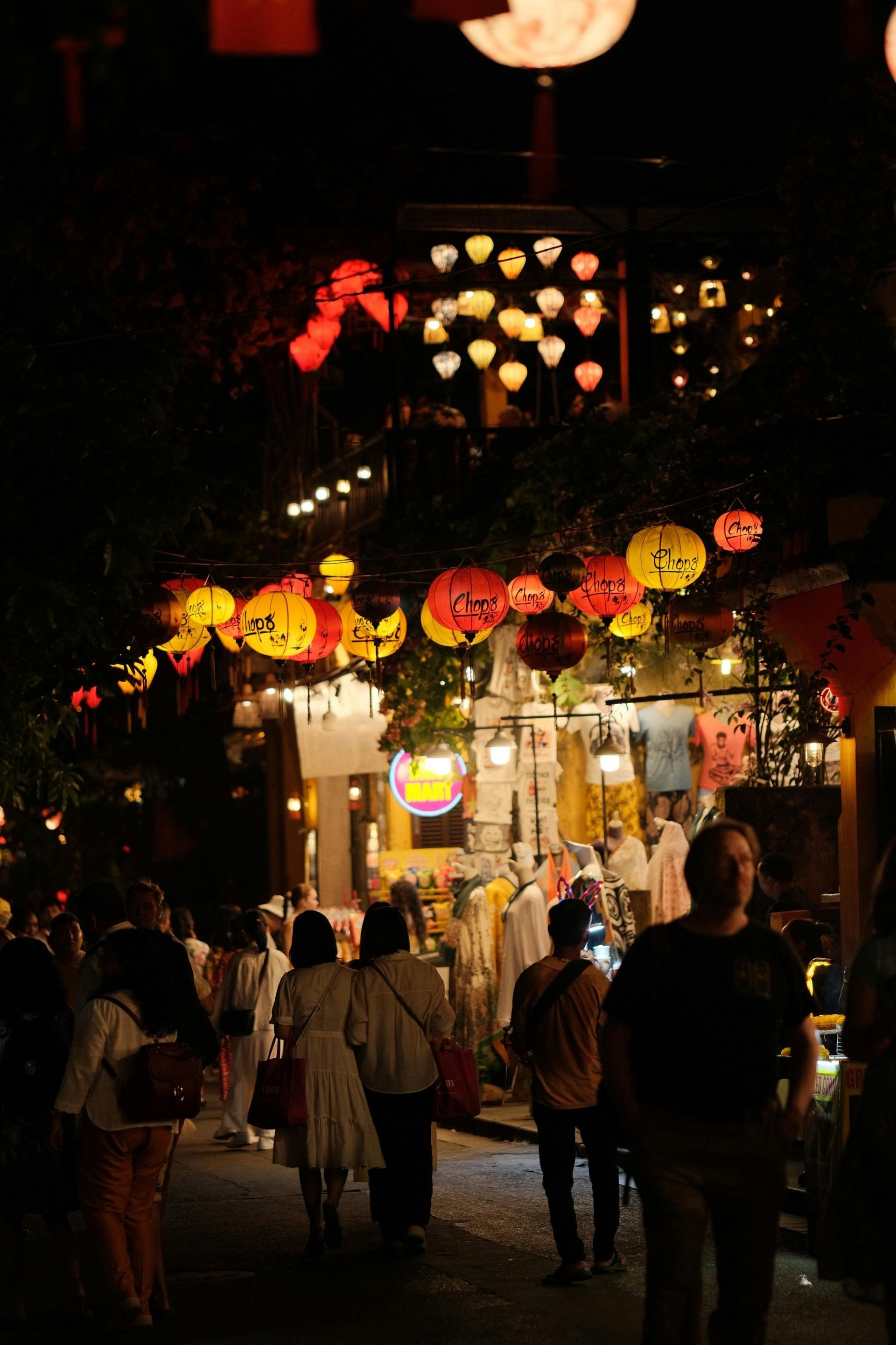 Night scene with illuminated lanterns over a crowded market street.