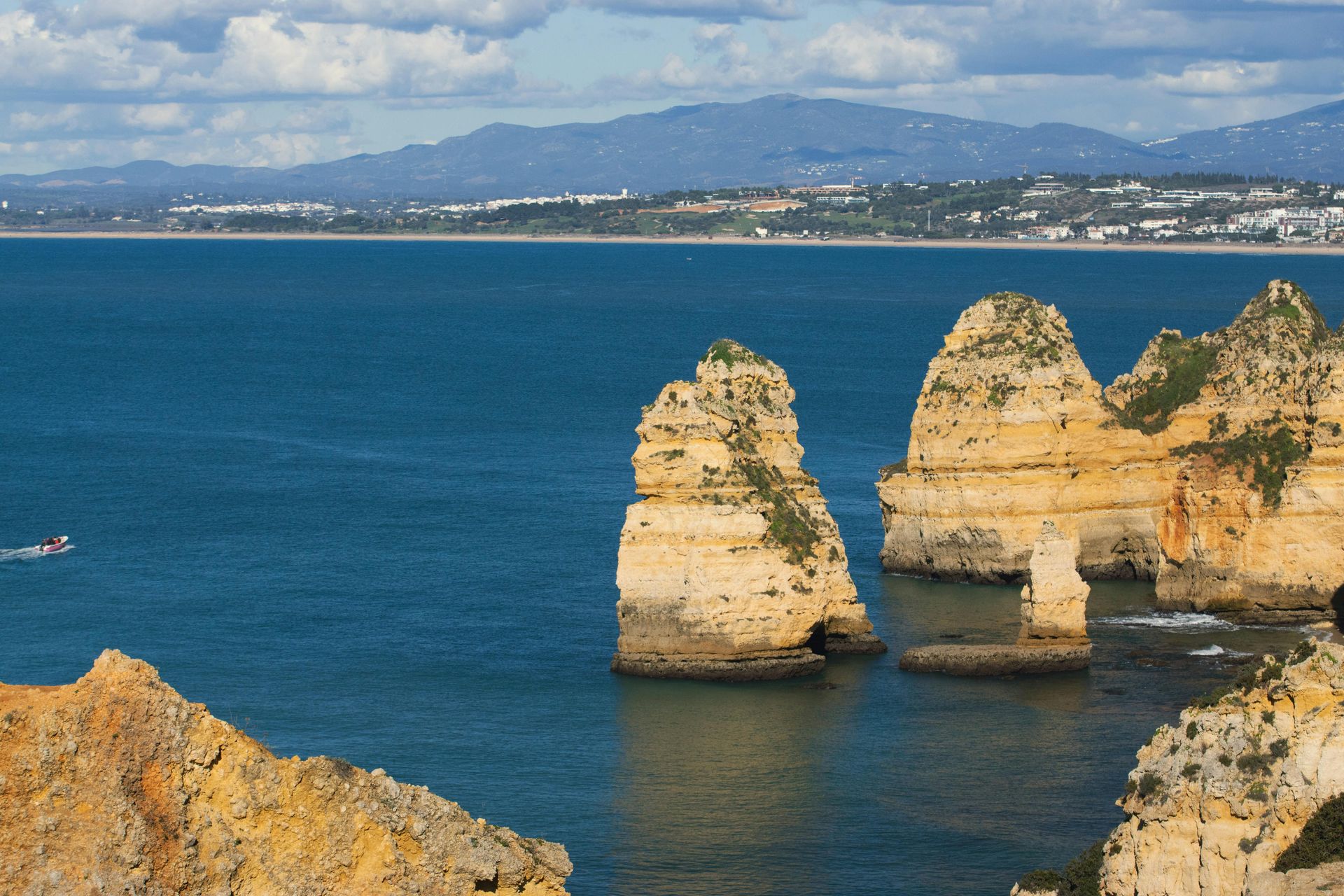 Cliffs rise from the turquoise sea in Lagos, Portugal, under a bright sky.