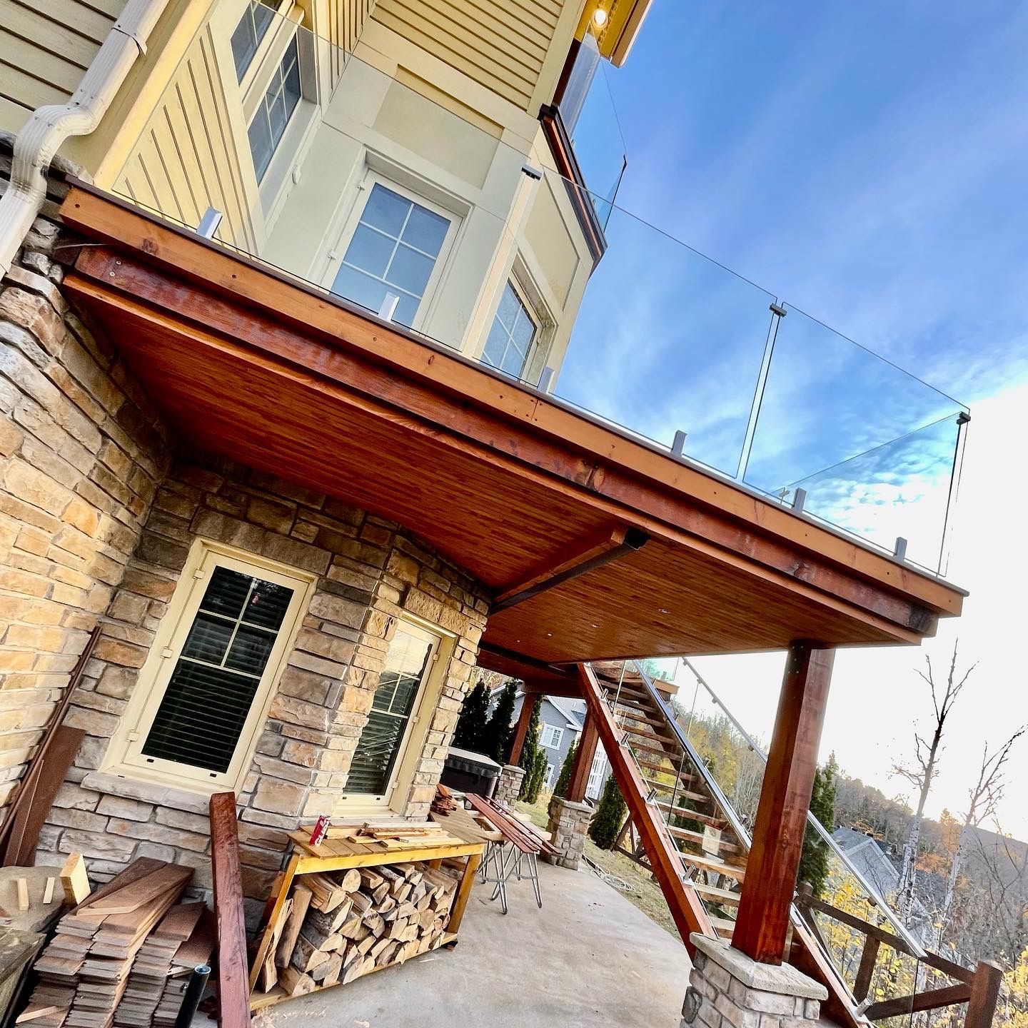 Une grande maison avec une terrasse en bois et une balustrade en verre.