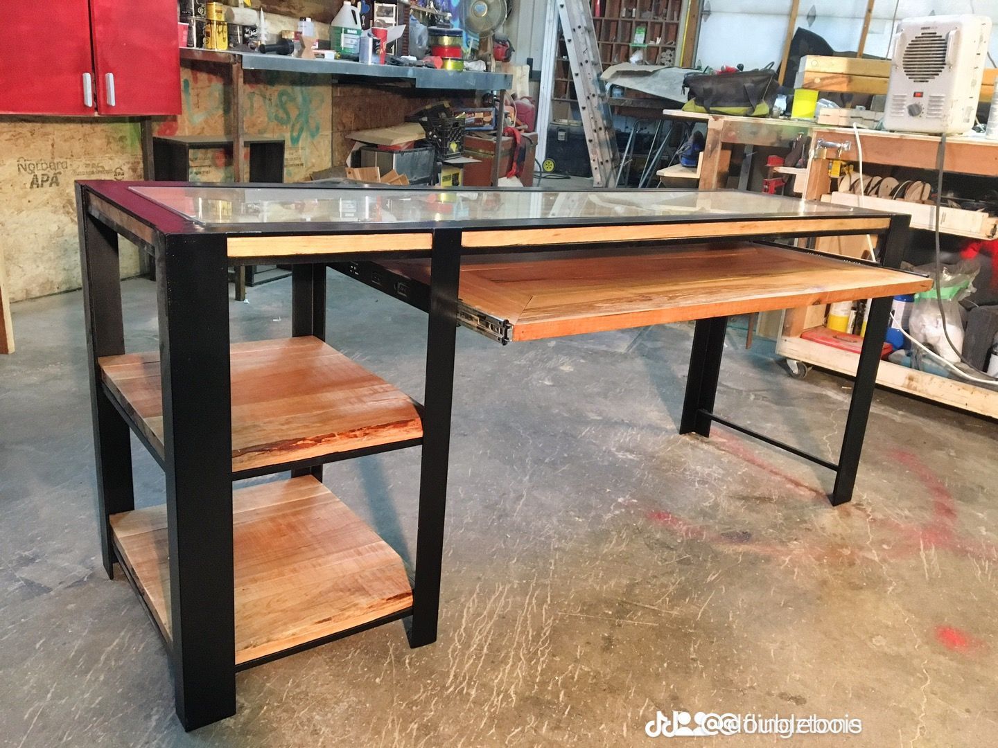 Une table en bois avec un plateau en verre et deux étagères dans un atelier.