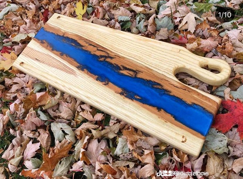 Une planche à découper en bois avec une poignée est posée sur un tas de feuilles.