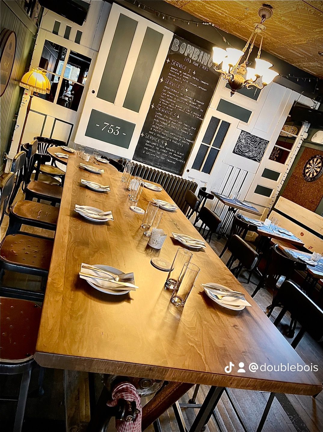 Une longue table en bois dans un restaurant avec des assiettes et des verres dessus.