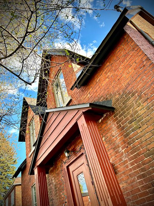 Un bâtiment en briques avec une porte rouge et un arbre en arrière-plan.