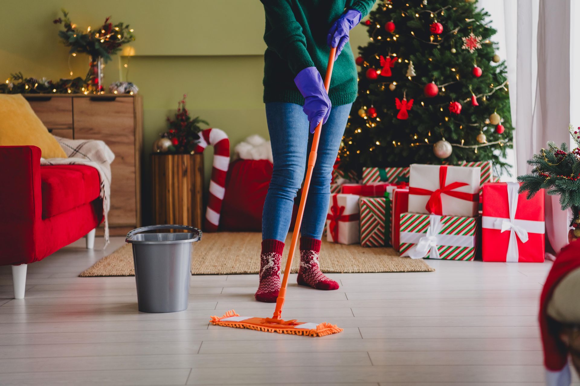 A woman is mopping the floor in front of a christmas tree.