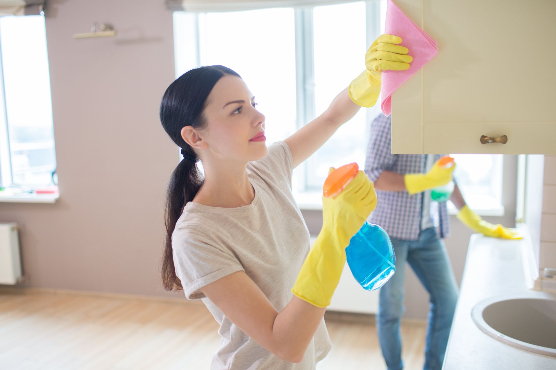 A woman is cleaning a cabinet in a kitchen while a man stands behind her.