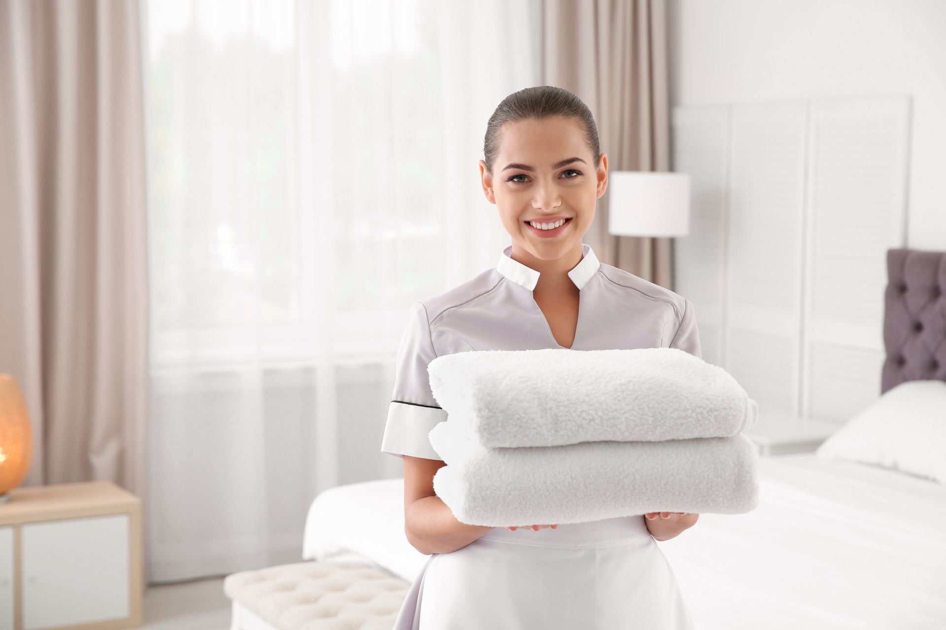A maid is holding a stack of towels in a hotel room.