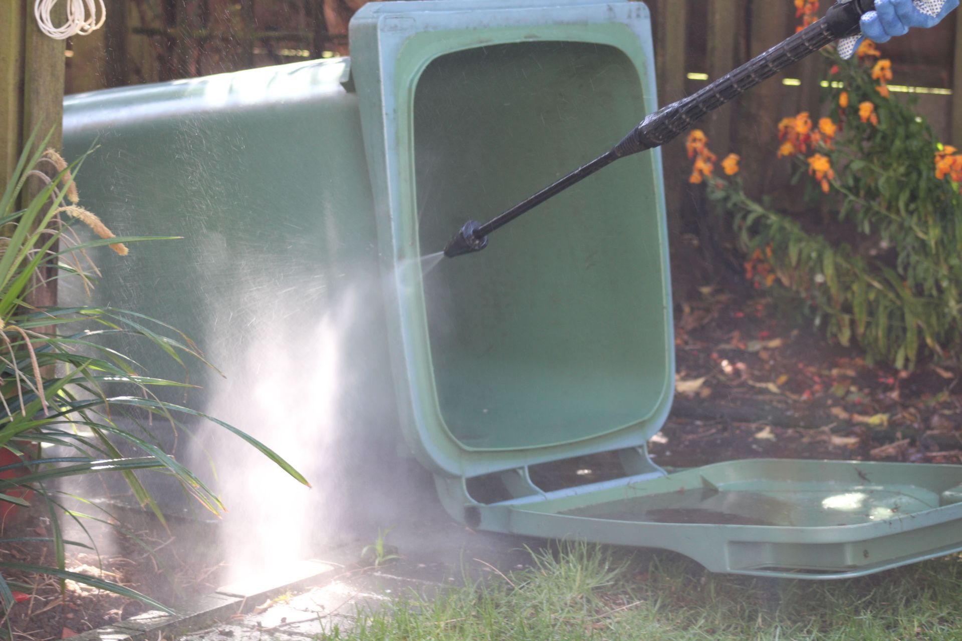 A person is cleaning a trash can with a high pressure washer.