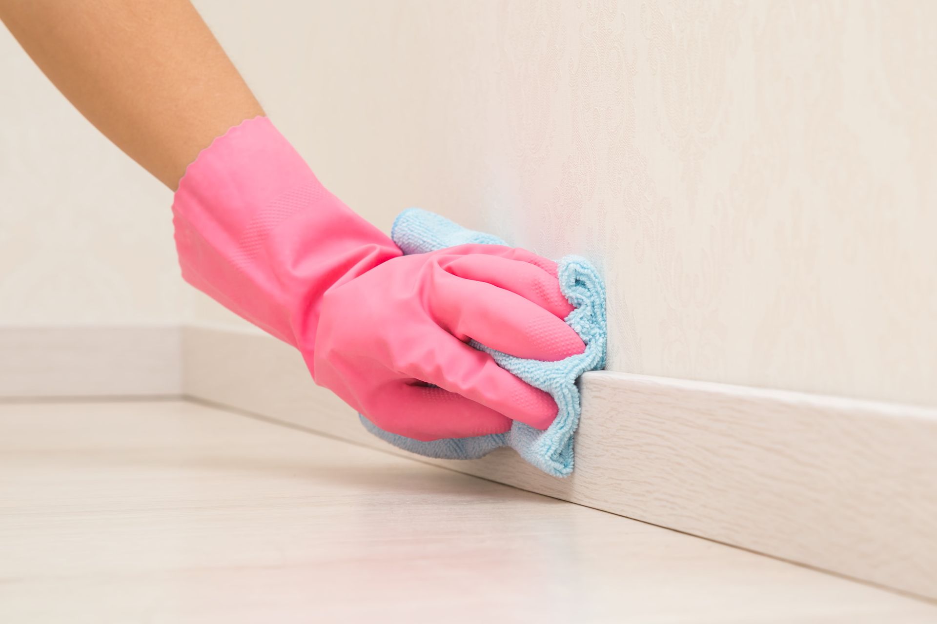 A person wearing pink gloves is cleaning a wall with a cloth.